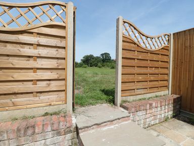 An open wooden garden gate with lattice top leading to a grassy field at The Old Dairy in Newnham-on-Severn