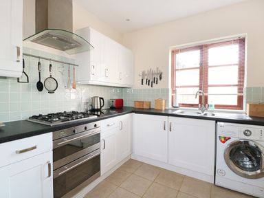 A kitchen with white cabinets black countertops a gas stove a washing machine and utensils hanging on the wall at The Old Dairy in Newnham-on-Severn
