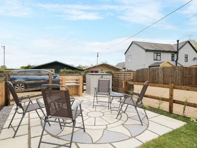 A patio area with four chairs and a small table on a circular patterned paved surface in a fenced backyard at The Nook in Royal Wootton Bassett