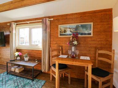 A wooden dining table with two chairs and a vase with flowers next to a coffee table with plants under a window at The Nook in Royal Wootton Bassett