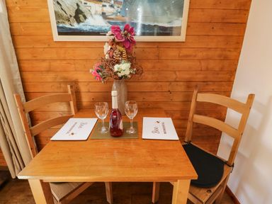 A wooden dining table with two chairs placemats glasses a bottle and a flower vase against a wooden wall at The Nook in Royal Wootton Bassett