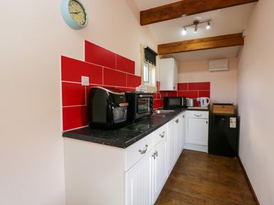 A kitchen with white cabinets black countertop red backsplash and appliances at The Nook in Royal Wootton Bassett