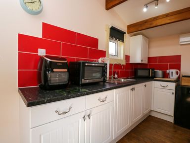 A kitchen with white cabinets red tile backsplash appliances and a wooden floor at The Nook in Royal Wootton Bassett