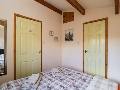 A bedroom with a bed covered in patterned bedding two closed doors a mirror and framed pictures on the wall at The Nook in Royal Wootton Bassett