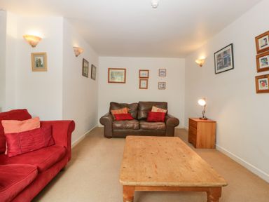A living room with a red sofa brown leather sofa wooden coffee table and side table with lamp at Wheelbarrow Cottage in Stoke Prior near Leominster