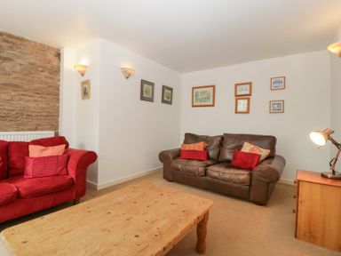 A living room with a red sofa a brown leather sofa a wooden coffee table and framed pictures on the wall at Wheelbarrow Cottage in Stoke Prior near Leominster