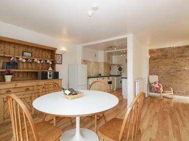 A dining area with a round table and wooden chairs next to a wooden hutch and an open kitchen at Wheelbarrow Cottage in Stoke Prior near Leominster