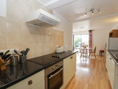 A kitchen with stovetop toaster kettle and utensils on counter leading to dining area with round table and chairs at Wheelbarrow Cottage Stoke Prior near Leominster