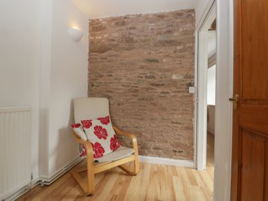 A corner of a room with a wooden chair and red floral cushions against a brick wall at Wheelbarrow Cottage in Stoke Prior near Leominster