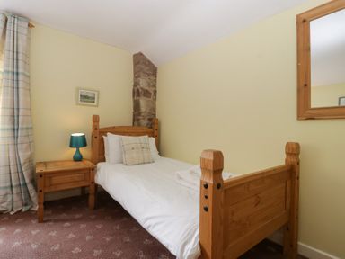 A bedroom with a wooden single bed a bedside table with a lamp a window with curtains and a wall mirror at Wheelbarrow Cottage in Stoke Prior near Leominster