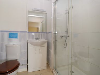 A bathroom with a toilet with a wooden seat a white sink with a cabinet a mirror and a glass shower enclosure at Wheelbarrow Cottage in Stoke Prior near Leominster