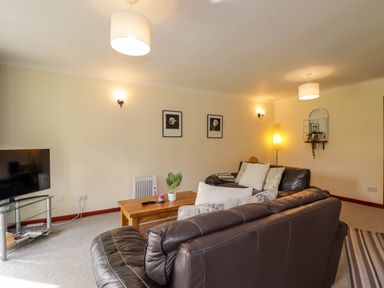 A living room with two brown leather sofas a wooden coffee table a television on a glass stand and framed pictures on the wall at Stone Water Cottage in Strathpeffer
