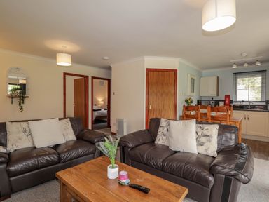 A living room with two brown leather sofas and a wooden coffee table in front of a kitchen area at Stone Water Cottage in Strathpeffer