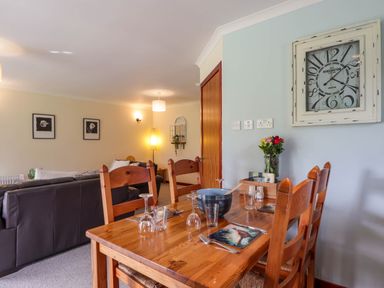 A dining table set with plates glasses and cutlery next to a living room with sofas and wall art at Stone Water Cottage in Strathpeffer
