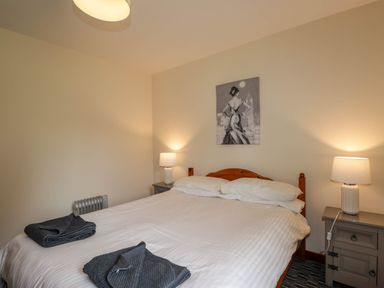 A bedroom with a double bed two bedside tables lamps and a painting above the bed at Stone Water Cottage in Strathpeffer