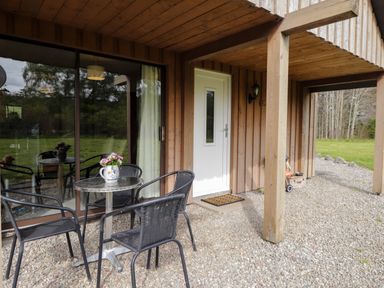 An outdoor seating area with a metal table and four black chairs next to a white door at Stone Water Cottage in Strathpeffer