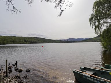 A lake with boats near a rocky shoreline and trees in the background at Stone Water Cottage in Strathpeffer