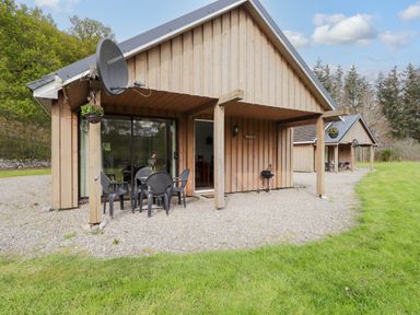 A wooden cabin with outdoor chairs and table on gravel near grass at Pebbles Cottage in Achilty near Strathpeffer