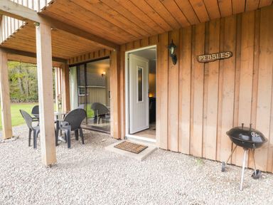 A covered outdoor area with a small table and four chairs a barbecue grill and an open door at Pebbles Cottage in Achilty near Strathpeffer