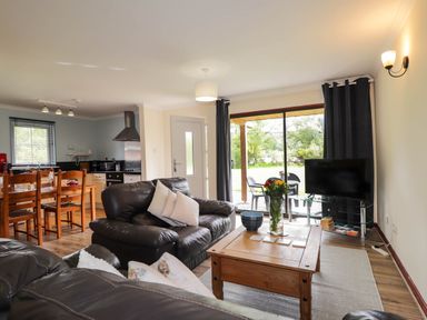 A living room with black leather sofas a wooden coffee table a television and dining table at Pebbles Cottage in Achilty near Strathpeffer