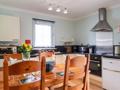 A kitchen with a wooden dining table and chairs a flower vase on the table and appliances on the counter at Pebbles Cottage in Achilty near Strathpeffer