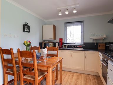 A kitchen with a wooden dining table and chairs next to cabinets and a window at Pebbles Cottage in Achilty near Strathpeffer