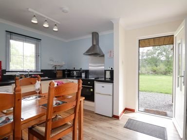 A kitchen with wooden dining table chairs window and door open to garden at Pebbles Cottage in Achilty near Strathpeffer