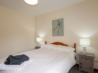 A bedroom with a double bed two bedside tables with lamps and a painting above the bed at Pebbles Cottage in Achilty near Strathpeffer