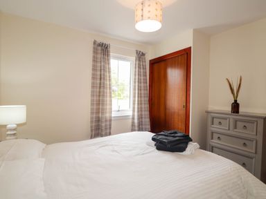 A bedroom with a bed a bedside lamp window with curtains a dresser with a vase and a closet with sliding wooden doors at Pebbles Cottage in Achilty near Strathpeffer