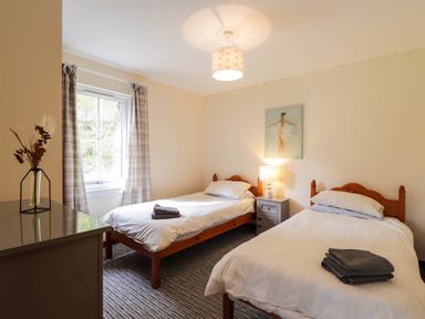 A bedroom with two single beds with white bedding and folded towels on top at Pebbles Cottage in Achilty near Strathpeffer