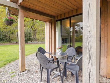A covered outdoor patio area with a round table and four plastic chairs at Pebbles Cottage in Achilty near Strathpeffer