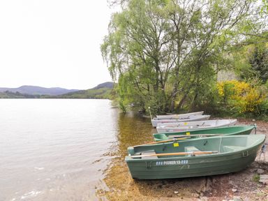 Rowboats docked on the shore of a lake with trees and hills in the background at Pebbles Cottage in Achilty near Strathpeffer