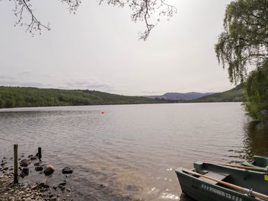 A lake with a small boat and trees on the shore at Pebbles Cottage in Achilty near Strathpeffer