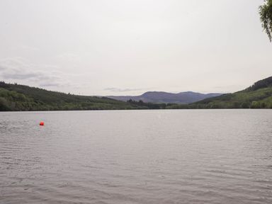 A lake with a red buoy surrounded by forested hills and mountains in the distance at Pebbles Cottage in Achilty near Strathpeffer