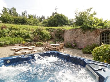An outdoor seating area with wooden picnic tables and chairs with a hot tub in the foreground at Wheelbarrow Castle in Leominster