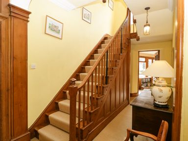 A hallway with wooden staircase carpet runner table lamp and framed pictures at Wheelbarrow Castle in Leominster