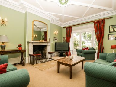 A sitting room with green armchairs red curtains a wooden coffee table and a fireplace at Wheelbarrow Castle in Leominster
