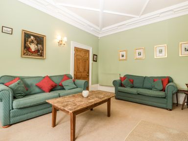 A sitting room with two green sofas a wooden coffee table and framed pictures on light green walls at Wheelbarrow Castle in Leominster