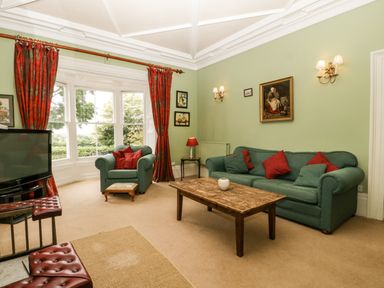A living room with green sofas red pillows a wooden coffee table red curtains and a television at Wheelbarrow Castle in Leominster