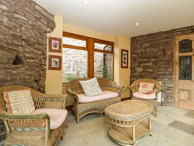 A room with wicker chairs a wicker table stone walls and wooden framed windows at Wheelbarrow Castle in Leominster