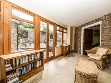 A room with wicker furniture and bookshelves next to large windows overlooking a patio at Wheelbarrow Castle in Leominster