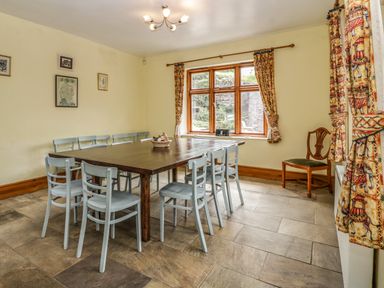 A dining room with a wooden table and several chairs by a window with patterned curtains at Wheelbarrow Castle in Leominster