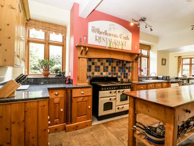 A kitchen with wooden cabinets a stove with tiled backsplash and a wooden island at Wheelbarrow Castle in Leominster
