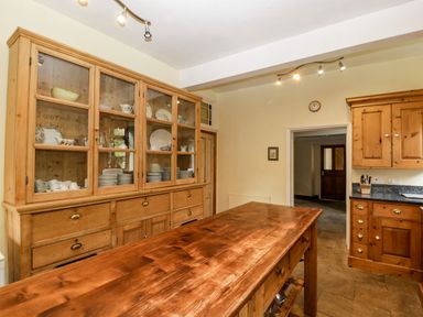 A kitchen with wooden cabinets a wooden island table and shelves with dishes at Wheelbarrow Castle in Leominster