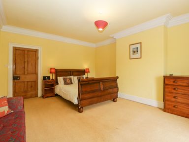 A bedroom with a wooden bed, bedside tables with lamps, a chest of drawers, and a patterned sofa at Wheelbarrow Castle in Leominster
