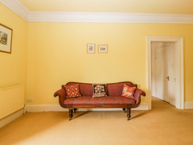 A yellow room with a red patterned wooden sofa and three cushions with framed pictures on the wall at Wheelbarrow Castle in Leominster