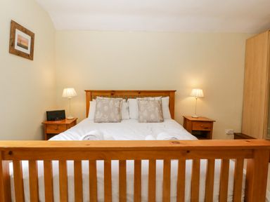 A bedroom with a wooden bed frame white bedding two bedside tables with lamps and a wardrobe at Wheelbarrow Castle in Leominster