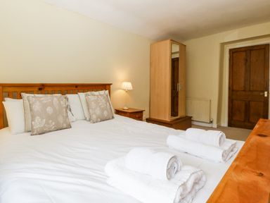 A bedroom with a wooden bed frame white bedding folded towels bedside table with lamp wooden wardrobe and wooden door at Wheelbarrow Castle in Leominster