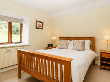 A bedroom with a wooden bed white bedding two bedside tables with lamps and a window at Wheelbarrow Castle in Leominster