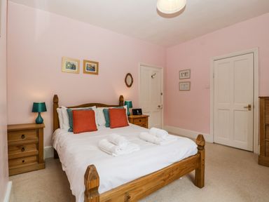 A bedroom with a wooden bed with white linens and rolled towels wooden bedside tables with lamps and framed pictures on pink walls at Wheelbarrow Castle in Leominster